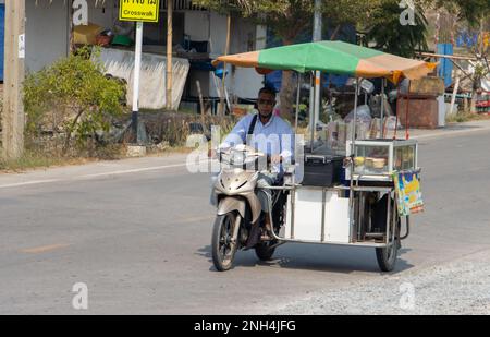 SAMUT PRAKAN, THAILANDIA, 01 2023 FEBBRAIO, un distributore di gelati cavalca una motocicletta a tre ruote lungo una strada del villaggio, Thailandia Foto Stock