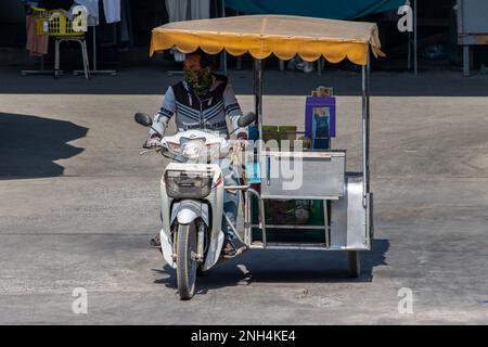 SAMUT PRAKAN, THAILANDIA, 13 2023 FEBBRAIO, un distributore di gelati cavalca una moto a tre ruote sulla strada soleggiata Foto Stock