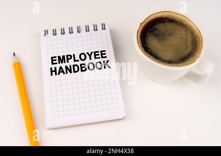 Concetto aziendale. Su una superficie bianca, una tazza di caffè, una matita e un blocco note con l'iscrizione - EMPLOYEE HANDBOOK Foto Stock