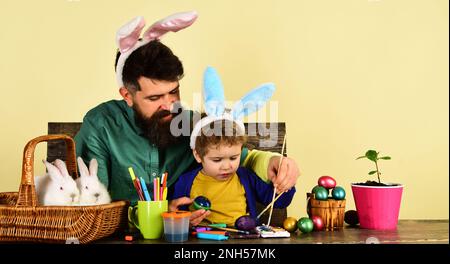 Padre e figlio dipingendo uova di Pasqua. Il giorno di Pasqua, un ragazzino carino che indossa le orecchie da coniglio. Felice Pasqua famiglia pittura uova per le vacanze. Padre Foto Stock