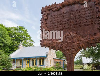 Arrugginito metallo informazioni storiche targa e vecchio 1841 fieldstone casa facciata con piante Hosta, fiori Hemerocallis al confine in estate. Foto Stock