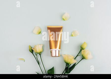 Tubo di crema dorata e fiori di eustoma bianco su sfondo azzurro. Vista dall'alto, piatto, mockup. Foto Stock