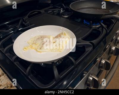 Uova fritte su media superficie, per colazione, in un piatto da pranzo bianco su un piano cottura. Foto Stock