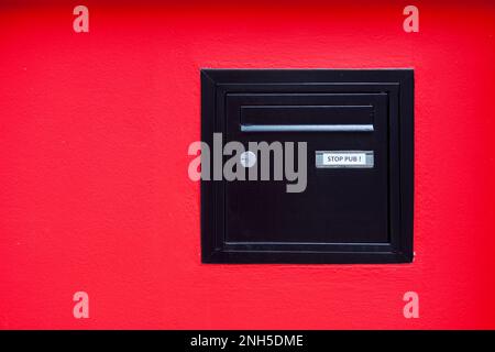Primo piano su una casella di posta nera incrostata in una parete rossa. Foto Stock