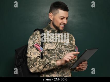 Cadet con zaino e tablet vicino alla lavagna. Educazione militare Foto Stock