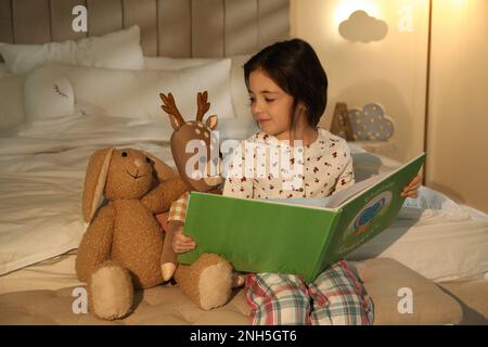 Piccola ragazza lettura libro in camera da letto illuminato da lampada da notte Foto Stock