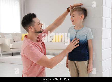 Padre che misura l'altezza del figlio vicino al muro di casa Foto Stock