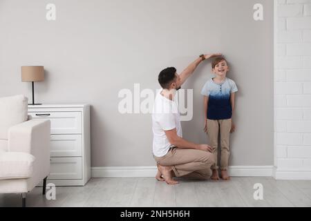 Padre che misura l'altezza del figlio vicino al muro di casa Foto Stock