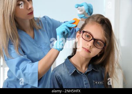 Medico che usa nit pettine e spray sui capelli della ragazza all'interno. Trattamento antighiaccio Foto Stock