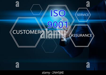 Uomo d'affari che punta all'icona virtuale con testo ISO 9001 su sfondo scuro, primo piano Foto Stock