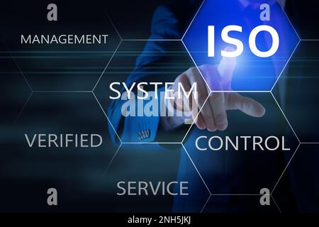 Uomo d'affari che punta all'icona virtuale con testo ISO su sfondo scuro, primo piano Foto Stock