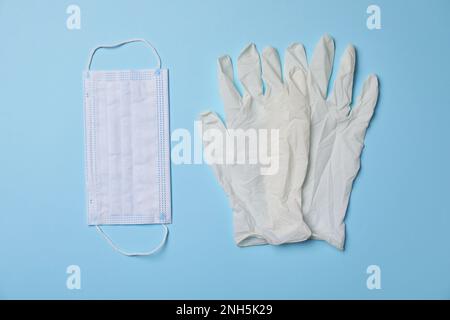 Guanti medici e maschera di protezione su sfondo azzurro, piatto. Attrezzatura di sicurezza Foto Stock