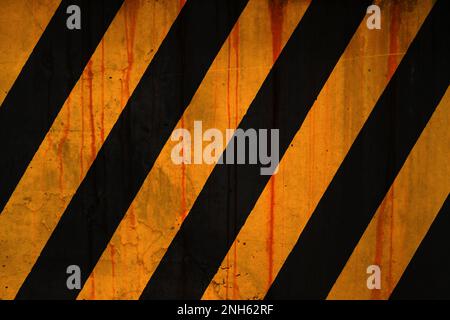 Parete in cemento intemperiato a telaio intero coperta da macchie di ruggine e vernice a strisce gialle e nere Foto Stock