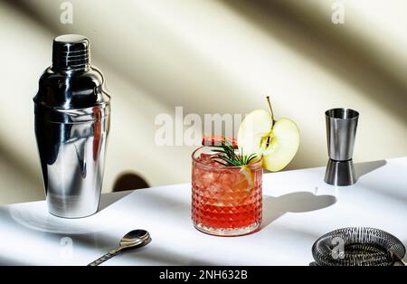 Bevanda alcolica di mele con vodka, liquore di mele, cannella, limone, guarnita con rosmarino. Sfondo beige chiaro, luce forte, ombra pat Foto Stock