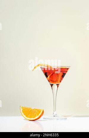 Cocktail Martinez con vermouth rosso, liquore, arancio amaro, scorza e ghiaccio. Sfondo beige chiaro, luce dura, motivo ombra, minimo Foto Stock