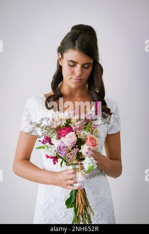 Il relativo non ogni giorno di sogno delle ragazze. Studio shot di una giovane sposa che tiene un mazzo di fiori su uno sfondo grigio. Foto Stock