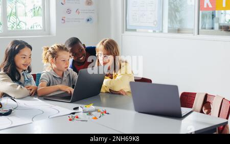 I bambini imparano a programmare i robot in una classe STEM basata su computer, lavorando insieme per costruire e azionare veicoli robotici. I bambini usano il computer così Foto Stock