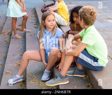 I tweenager positivi si fanno baffare mentre si siedono sui gradini all'aperto Foto Stock