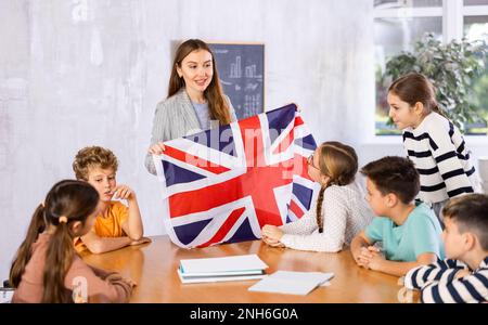 Insegnante che parla della bandiera nazionale e nazionale della Gran Bretagna alla lezione di Geografia. Gli scolari e le insegnanti di sesso femminile discutono positivamente Foto Stock