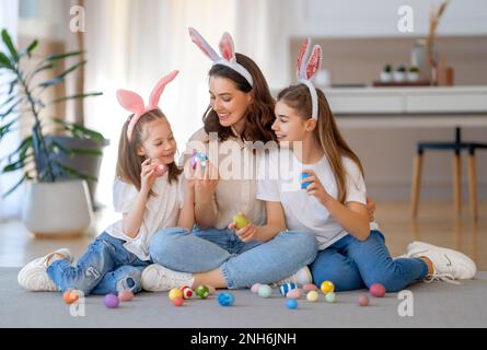 Buona vacanza. Madre e le sue figlie con uova da pittura. La famiglia festeggia la Pasqua. Le ragazze cute dei bambini stanno portando le orecchie conigliate. Foto Stock