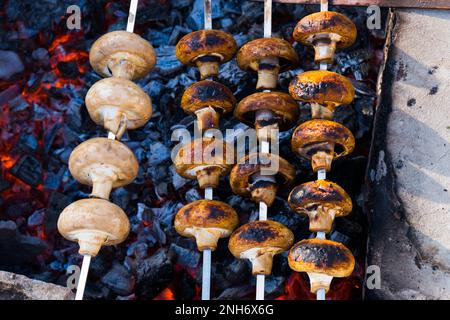 Il barbecue Shampynon è fritto su carbone. Preparazione di funghi alla griglia su spiedini, crudi e pronti. Cibo sul fuoco. Foto di alta qualità Foto Stock