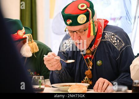 Riedlingen, Germania. 21st Feb, 2023. Kretschmann, primo ministro di Baden-Württemberg (centro, i Verdi/Bündnis 90, M), mangia un piatto di rana trippa al Municipio il martedì Shrove. Più di 300 stolti della gilda Gole 1865 partecipano al fumo di sigaro, al pasto di Froschkuttel del 192nd e alla successiva uscita dal municipio, e in seguito intendono giocare attraverso la città. La rana trippa è una specialità di Riedlingen. Si affettava lo stomaco di manzo sott'aceto. Credit: Felix Kästle/dpa/Alamy Live News Foto Stock