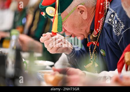 Riedlingen, Germania. 21st Feb, 2023. Kretschmann, primo ministro di Baden-Württemberg (centro, i Verdi/Bündnis 90, M), mangia un piatto di rana trippa al Municipio il martedì Shrove. Più di 300 stolti della gilda Gole 1865 partecipano al fumo di sigaro, al pasto di Froschkuttel del 192nd e alla successiva uscita dal municipio, e in seguito intendono giocare attraverso la città. La rana trippa è una specialità di Riedlingen. Si affettava lo stomaco di manzo sott'aceto. Credit: Felix Kästle/dpa/Alamy Live News Foto Stock