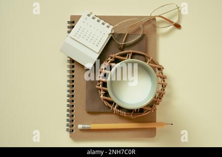 Notebook marrone, calendario, occhiali, tazza di latte, matita su sfondo giallo. piano di giacitura, vista dall'alto Foto Stock