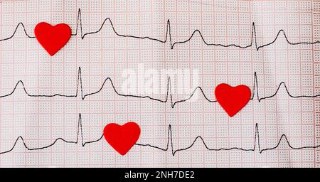 Cuori rossi su un cardiogramma, un simbolo del battito cardiaco. Primo piano di un elettrocardiogramma su carta. Concetto sanitario e medico. Spazio di copia Foto Stock