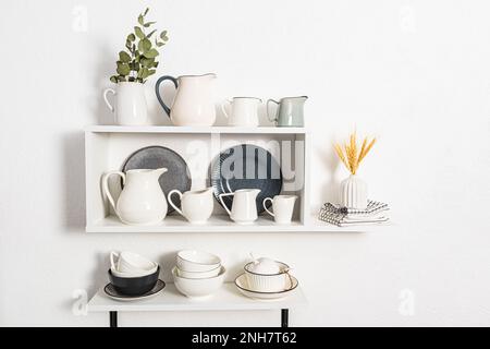 molte caraffe diverse sotto l'acqua e il latte sono sulle mensole aperte della cucina. ciotole e piatti. Bella vista interna bianca degli scaffali della cucina Foto Stock