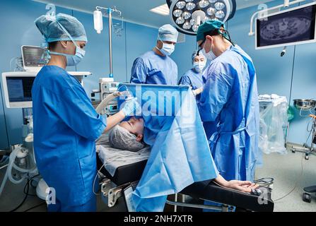 Team di chirurghi e infermieri che eseguono interventi chirurgici in sala operatoria ospedaliera. Chirurgia Foto Stock