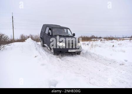 Russo nero 4x4 SUV in vernice protettiva Raptor 'UAZ Patriot Pickup' si sposta rapidamente da una banca della neve in inverno. Foto Stock