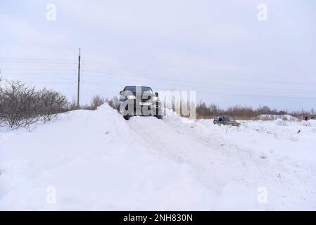 Il SUV russo 'UAZ Patriot' procede rapidamente su una strada innevata nel campo in inverno sullo sfondo della foresta aggrappata alla ruota della tempesta di neve. Foto Stock