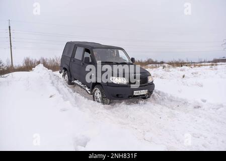 Russo nero 4x4 SUV in vernice protettiva Raptor 'UAZ Patriot Pickup' si sposta rapidamente da una banca della neve in inverno. Foto Stock