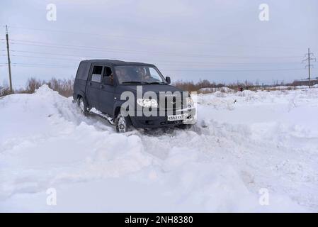 Russo nero 4x4 SUV in vernice protettiva Raptor 'UAZ Patriot Pickup' si sposta rapidamente da una banca della neve in inverno. Foto Stock