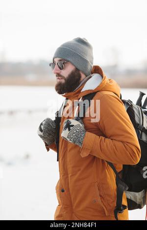 Un uomo bearded con uno zaino in abiti caldi di inverno sta camminando su un lago ghiacciato in inverno. Il concetto di trekking e di stile di vita attivo. Foto Stock