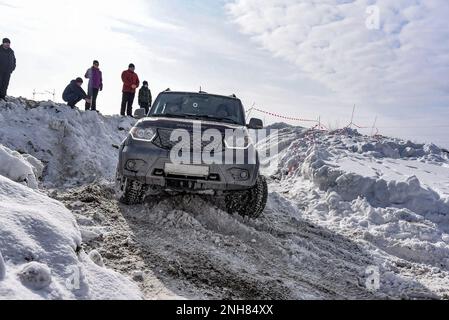 Il SUV russo 'UAZ Patriot' va rapidamente su una strada innevata nel campo in inverno, aggrappandosi alla ruota paracolpi. Foto Stock