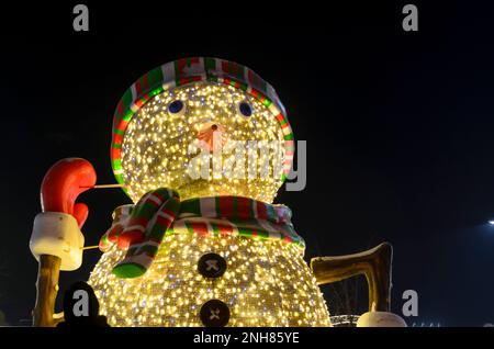 Luci da neve colorate e brillanti con berretto a righe e sciarpa, bottoni neri e naso di carota hanno fatto salire una mano accogliente nei guanti. Foto Stock