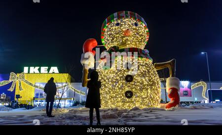 Donna che fotografa un uomo nel negozio 'IKEA' in inverno, vicino a un pupazzo di neve incandescente. Decorazione natalizia delle strade vicino al negozio 'Mega' a Novosibir Foto Stock