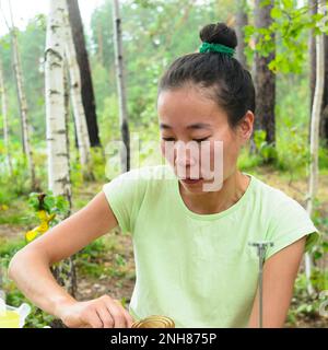 La ragazza asiatica con gli occhi downcast facendo qualcosa mani al tavolo all'aperto. Foto Stock