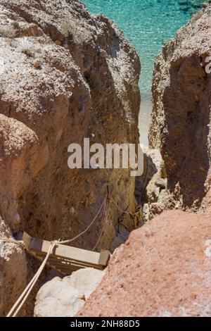 Stretto passaggio con scala in legno per scendere alla spiaggia di Tsigrado, Milos Foto Stock