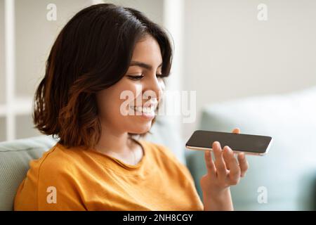 Primo piano ripresa di una giovane donna araba sorridente che registra un messaggio vocale su smartphone Foto Stock