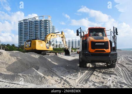 Un escavatore si trova sulla cima di un grande mucchio di sabbia e carica la sabbia su un camion di scarico presso l'Indian Beach Park di Miami, Florida, Stati Uniti L'Army Corps of Engineer continua a lavorare al progetto di Miami Beach Renourishment che distribuisce il posizionamento della sabbia all'estremità meridionale dell'Indian Beach Park e di Allison Beach. Foto Stock
