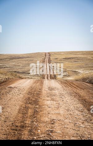 Una strada sterrata che conduce in lontananza e su una lontana collina all'orizzonte sotto un cielo azzurro chiaro. Foto Stock