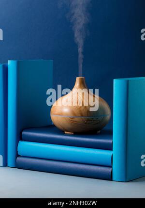 fragranza di legno sul tavolo da lavoro con vapori di essenza di oli naturali, con libri di colore blu e teal Foto Stock