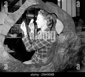 Donna in posa con il meteorite Irwin-Ainsa (anello di Tucson) al Museo Smithsonian di Storia Naturale, Washington, D.C. Questo meteorite di Tucson è un frammento di meteorite brezinaite. Fu rivendicata dai missionari gesuiti ai piedi della Sierra de la Madera negli anni '1700s e poi trasportata a Tucson, Arizona, dove fu usata come una sorta di incudine pubblica. La Brezinaite è un raro minerale composto da cromo e zolfo, presente nelle meteoriti. Harris & Ewing, fotografo, c. 1938-39. Foto Stock