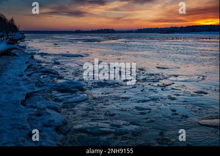 Ghiaccio coperto di neve sull'acqua ghiacciata del fiume un tramonto. Sfondo blu scuro naturale. Foto Stock