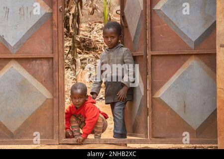 Karatu, Tanzania - 16th ottobre 2022: Due bambini alla loro porta di cortile a Karatu, Tanzania. Ci sono sei dita sulla mano sinistra del ragazzo. Foto Stock