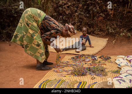 Karatu, Tanzania - 16th ottobre 2022: Una donna locale che prepara la sua merce per la vendita nel suburbano Karatu, Tanzania, mentre suo figlio si accinge. Foto Stock