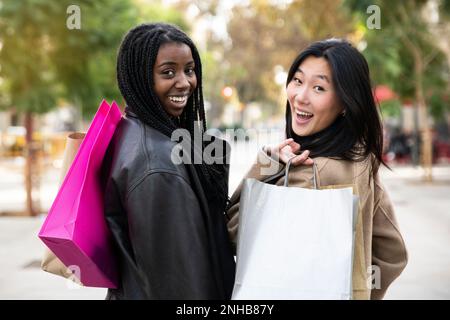 Vista posteriore di due donne che camminano per strada per lo shopping - concetto di amicizia multirazziale della gente Foto Stock